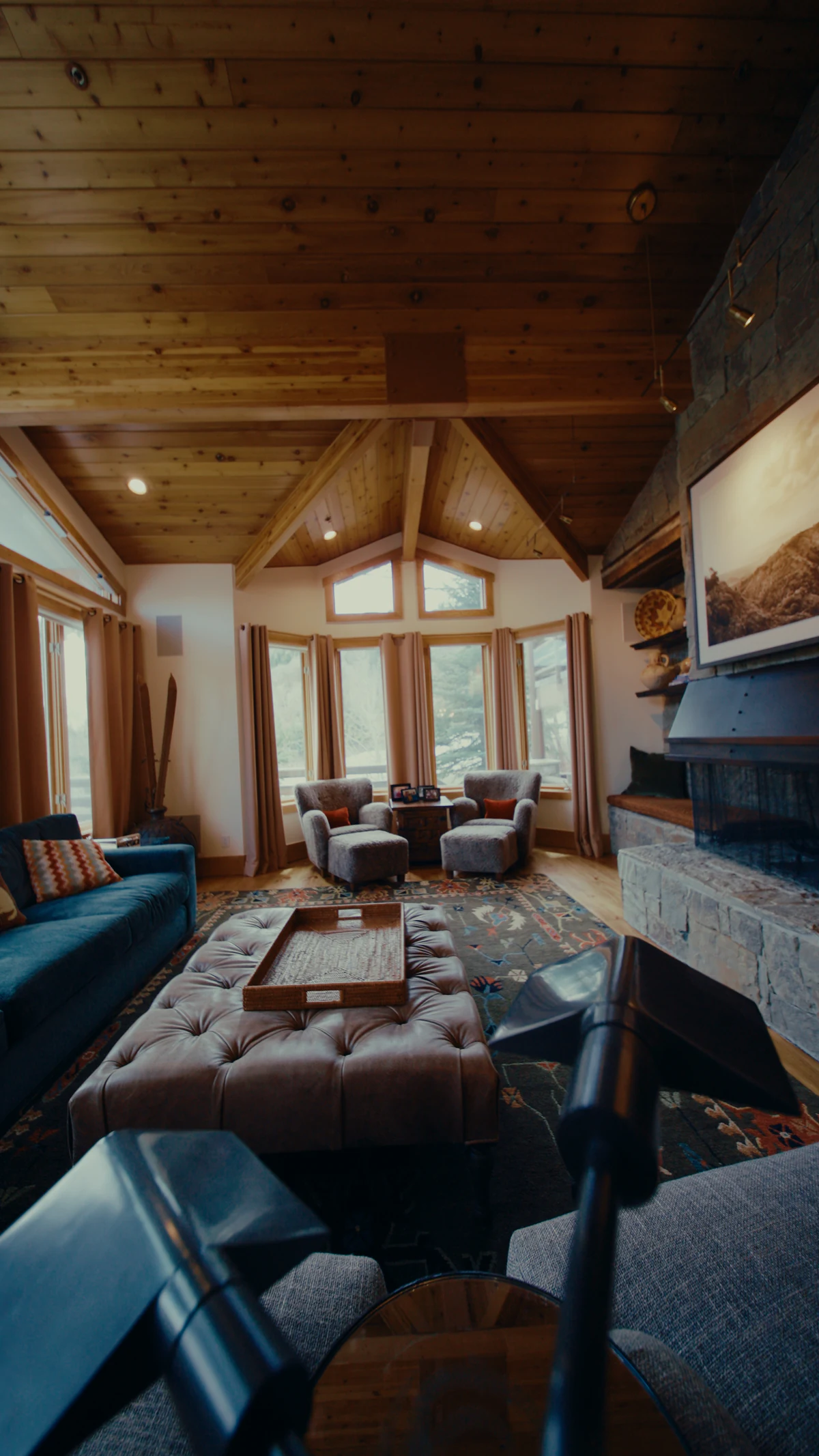 A mountain cabin living room with a wood ceiling and stone fireplace.