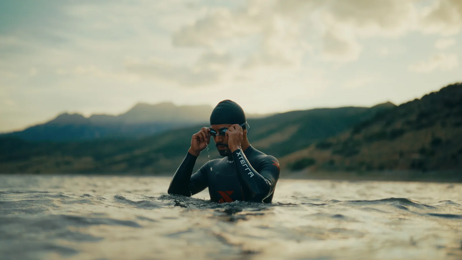 A swimmer adjusting his goggles in a mountain lake.