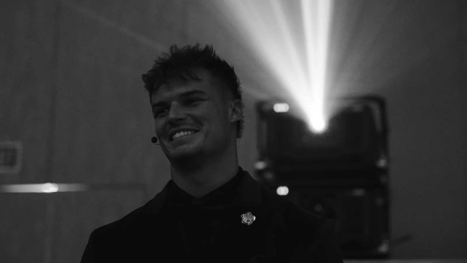 A speaker smiling on stage with a projector beam behind him.